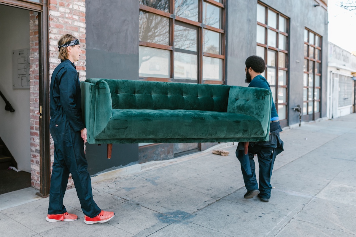 Two movers carrying an old sofa out of a house